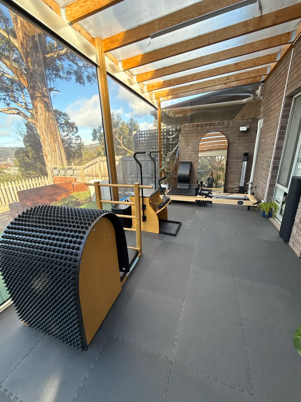 Sunlit studio with ladder barrel, chair and reformer under a timber-framed glass roof